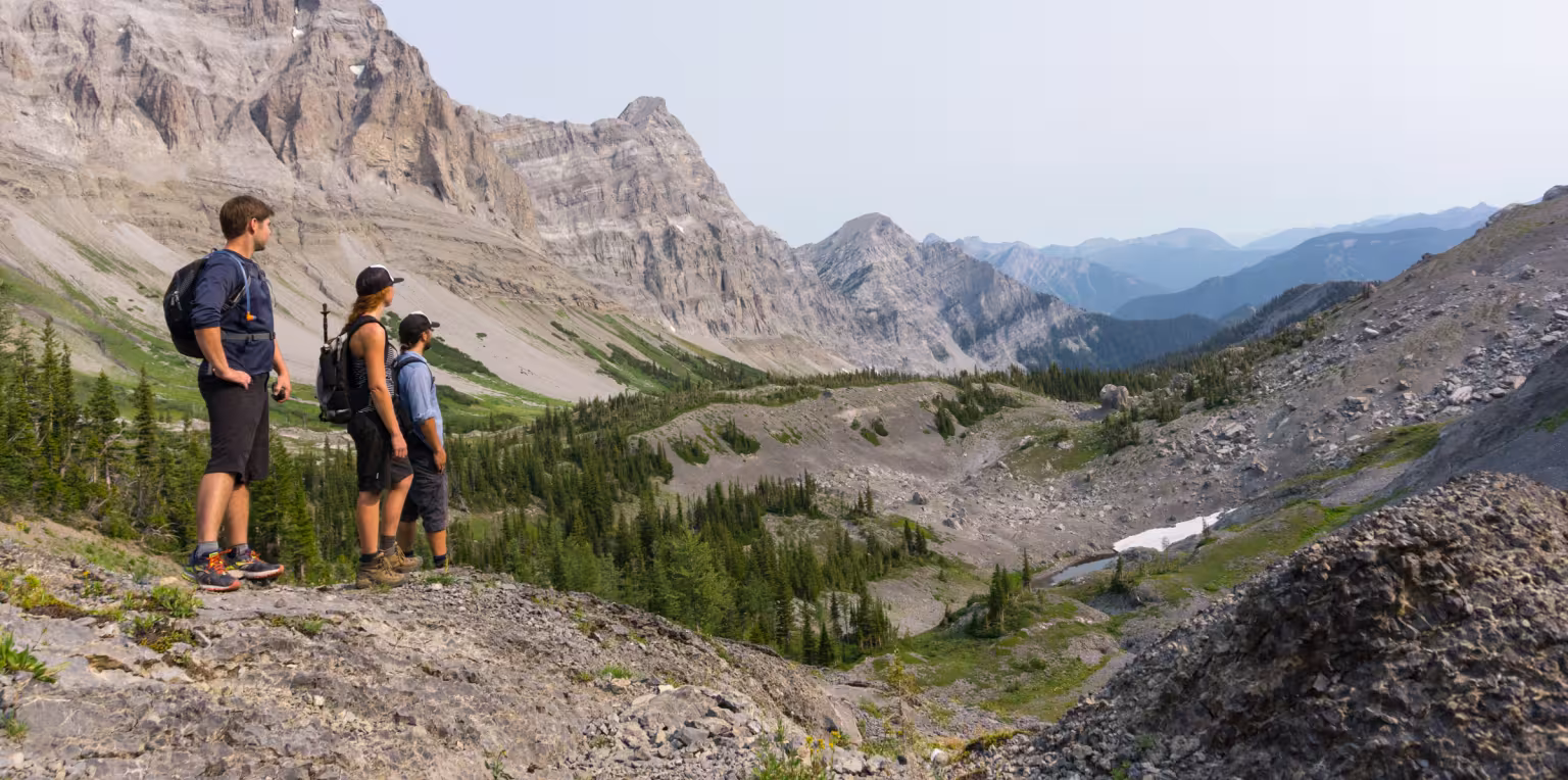 Two hikers standing on rocky mountain trail overlooking valley.
