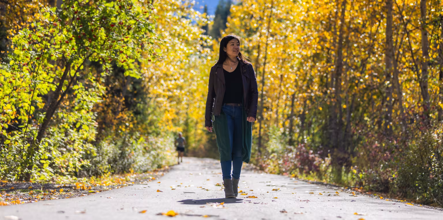 Woman walking down a leafy forest path, surrounded by yellow trees.