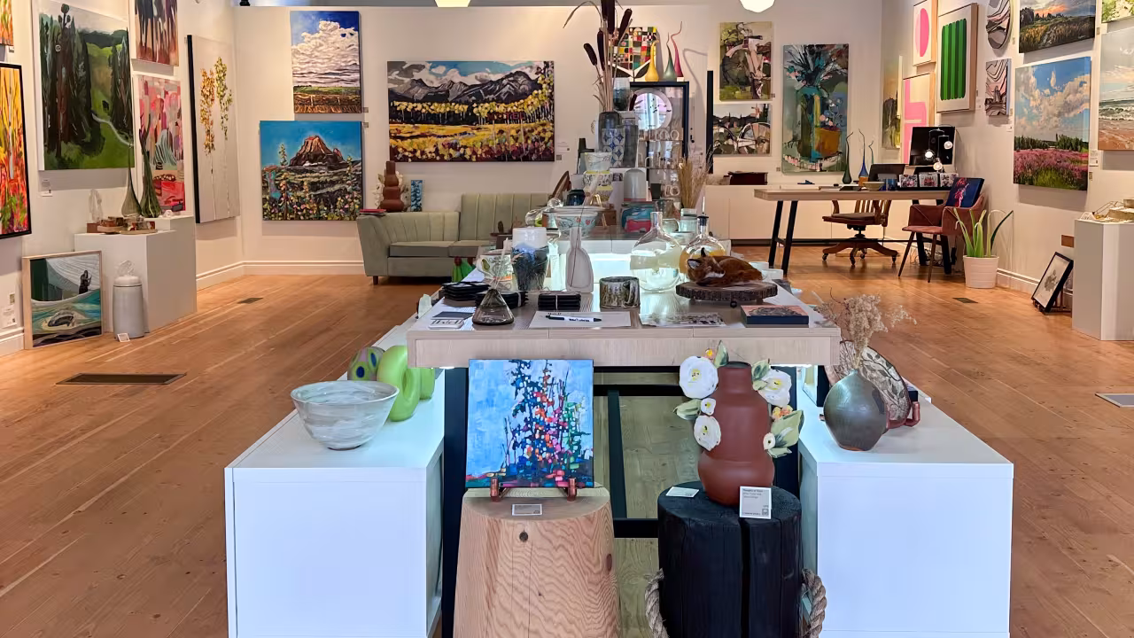 Large white table with paintings, pottery and glass art pieces displayed. 