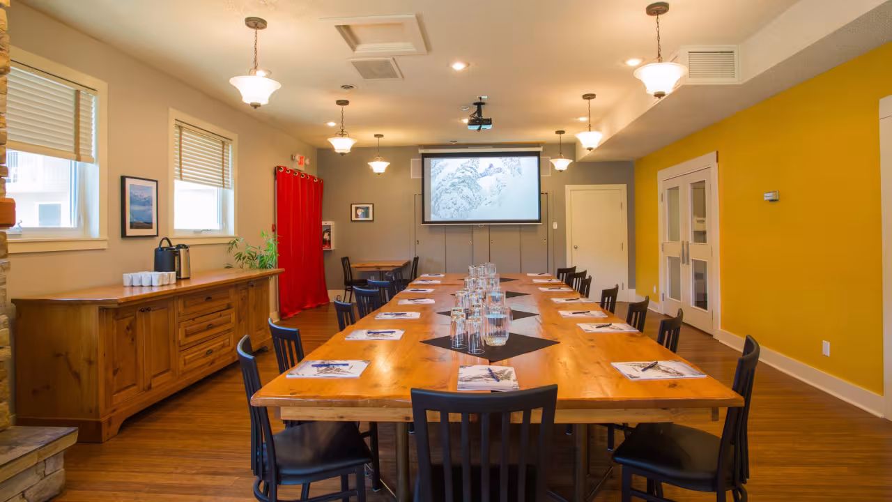 Meeting room with large table set with papers, pens and water glasses,, screen, projector, and red curtains