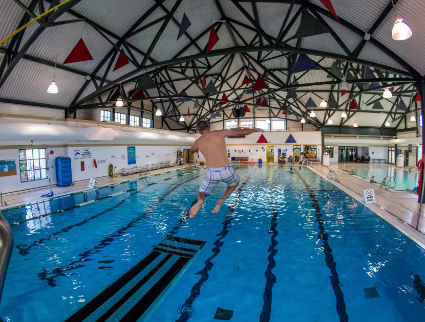 Swimmer diving into an indoor lap pool with people in background.