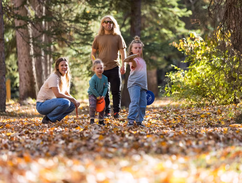 Family walking through autumn leaves in a forest, smiling.