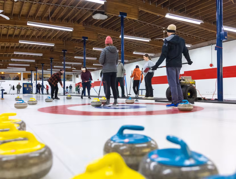 People playing curling on indoor ice rink with colorful stones.