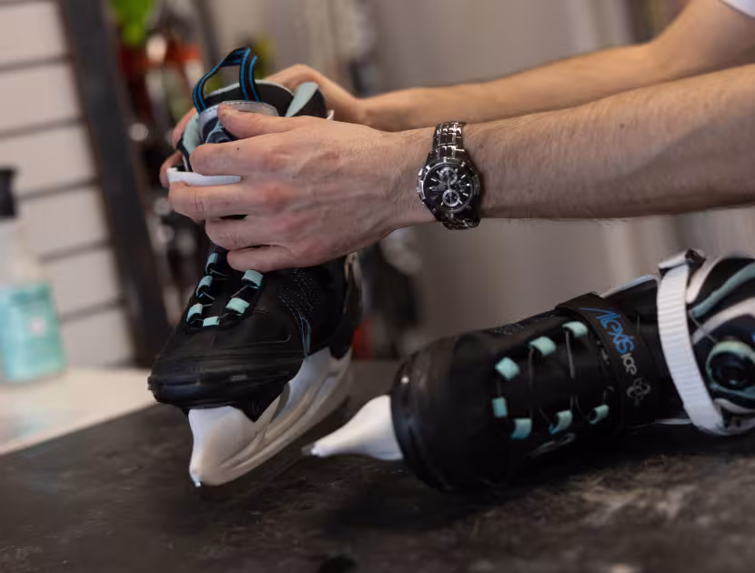 Man tying black ice skates on a table.