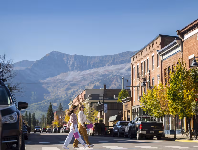 People walking across a street in a small town with mountains in the background.