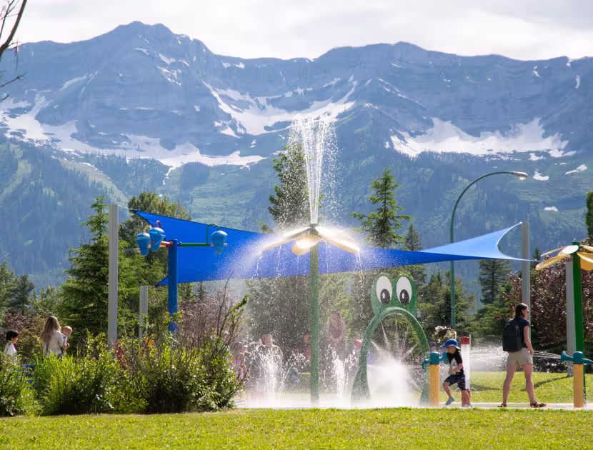 Children playing in outdoor water park with a Rocky Mountain backdrop..