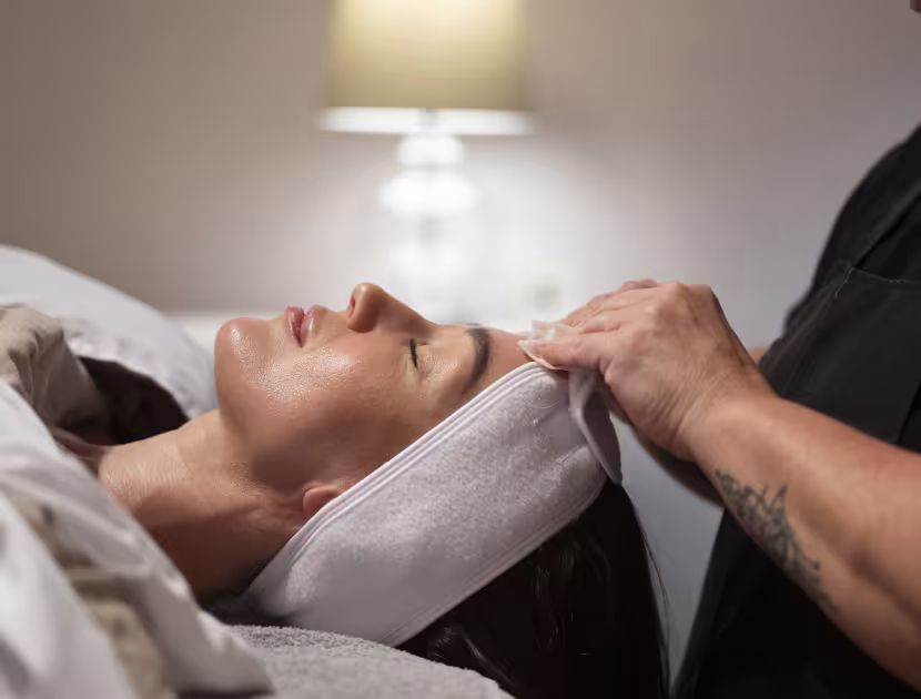 Woman receiving facial treatment, therapist's hands on face.