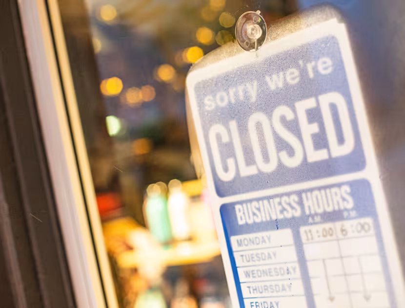 Blue and white closed sign on a storefront door; blurred lights in background.