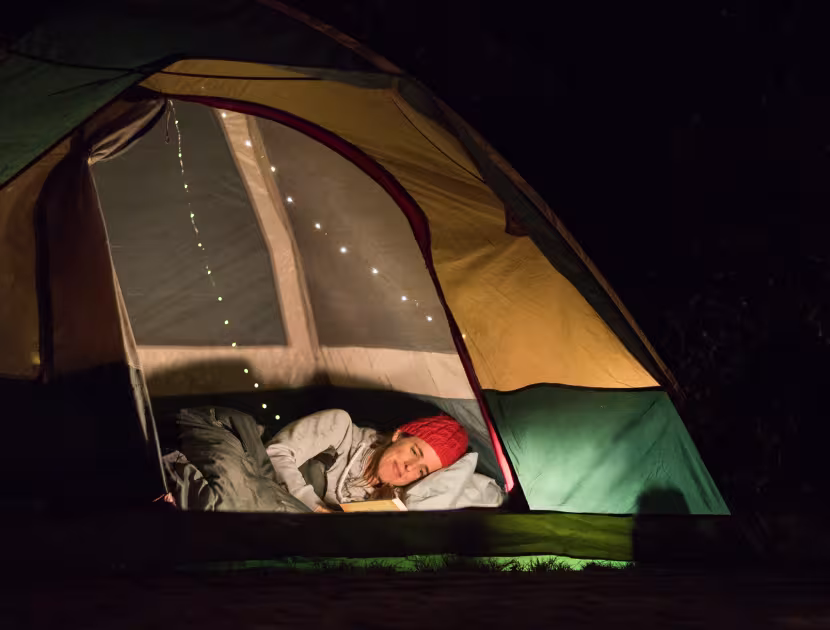 Shot of a woman reading a book at night while lying in a tent.