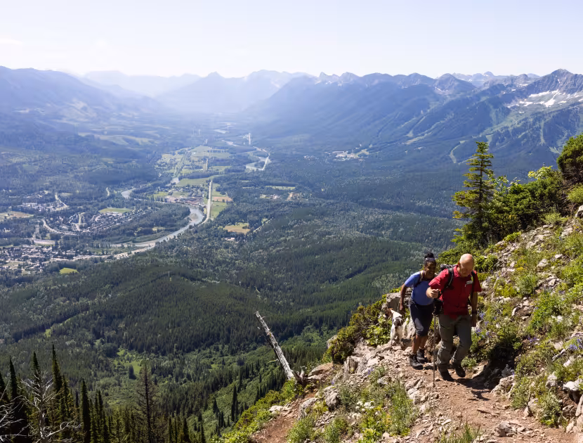 Hikers on mountain trail overlooking valley and mountains.