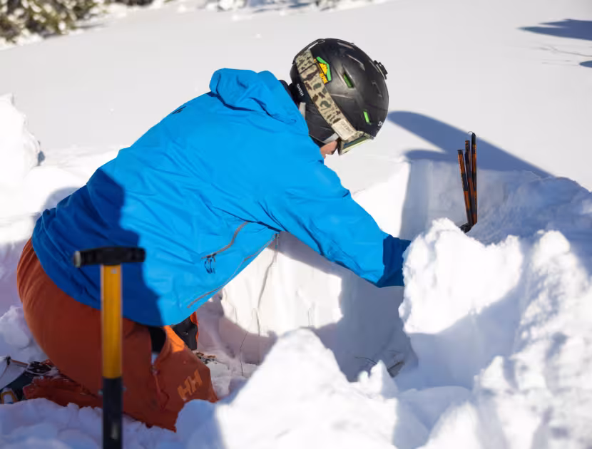 Person in blue jacket and orange pants digging in snow with shovel.
