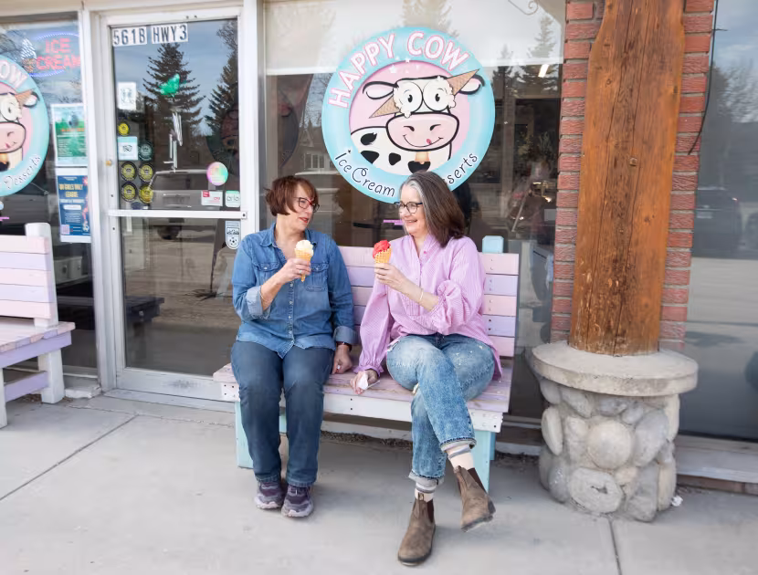 Two women eating ice cream outside an ice cream shop, smiling and enjoying treats.