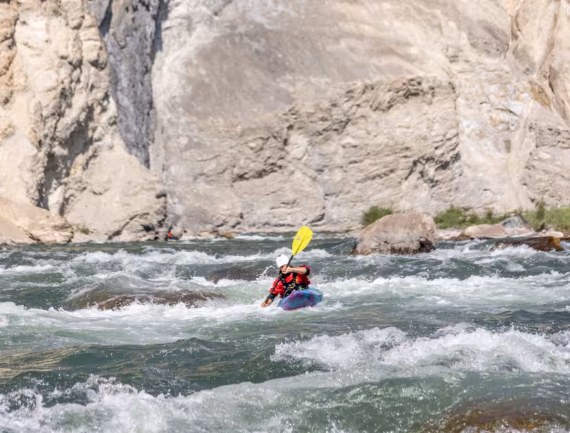 Person kayaking on a river with a large rocky cliff in the background.