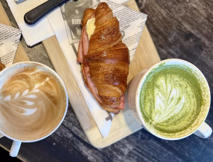 Two croissants and two coffee drinks on wooden boards.