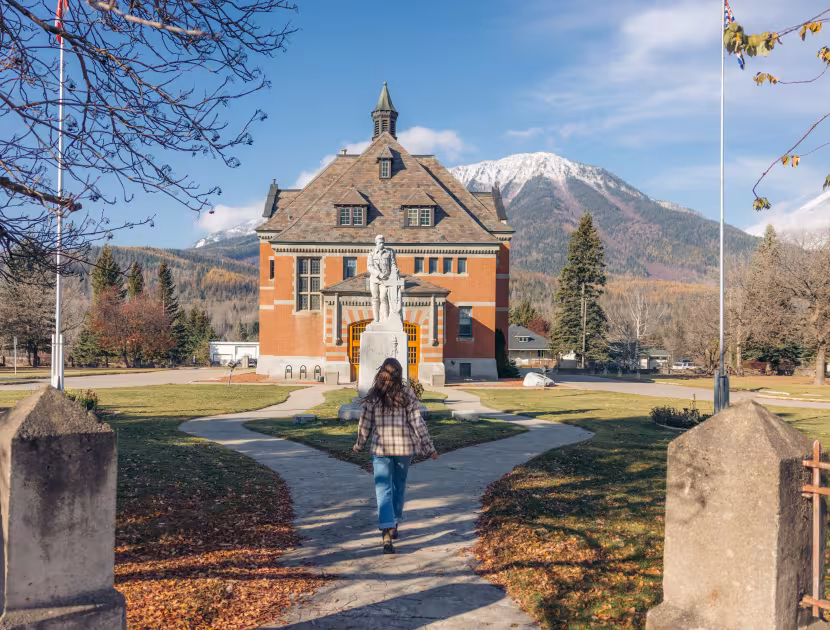 Woman walking on path to red brick building with mountains in background.