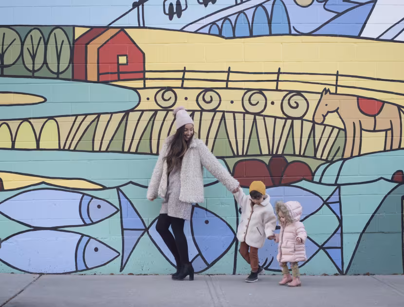 Woman and toddler holding hands in front of colorful mural.