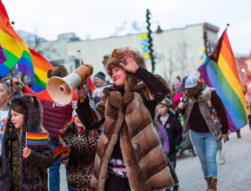 People marching in a Pride parade, waving rainbow flags and cheering.