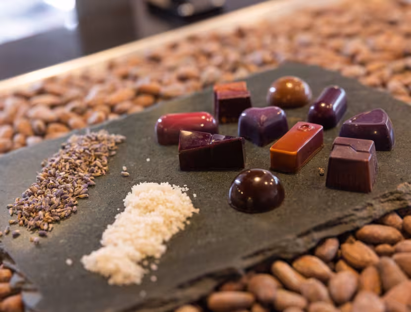 Assorted chocolates on a slate plate with two piles of toppings, on a background of coffee beans.