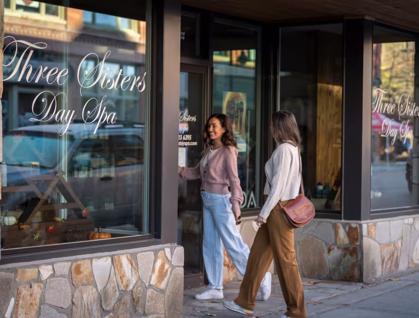 Two women walking into a day spa with stone facade and large windows.