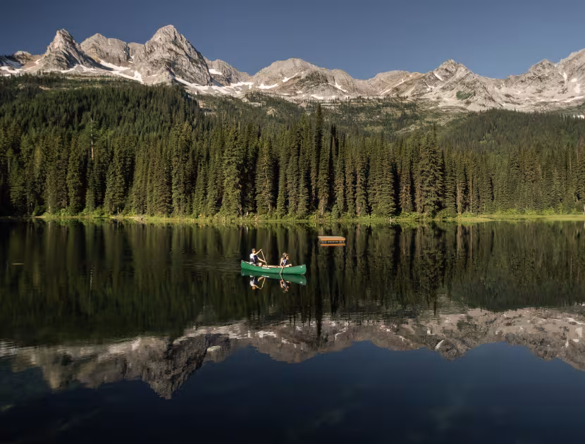 A serene lake reflecting trees and snow-capped mountains, with two kayaks.