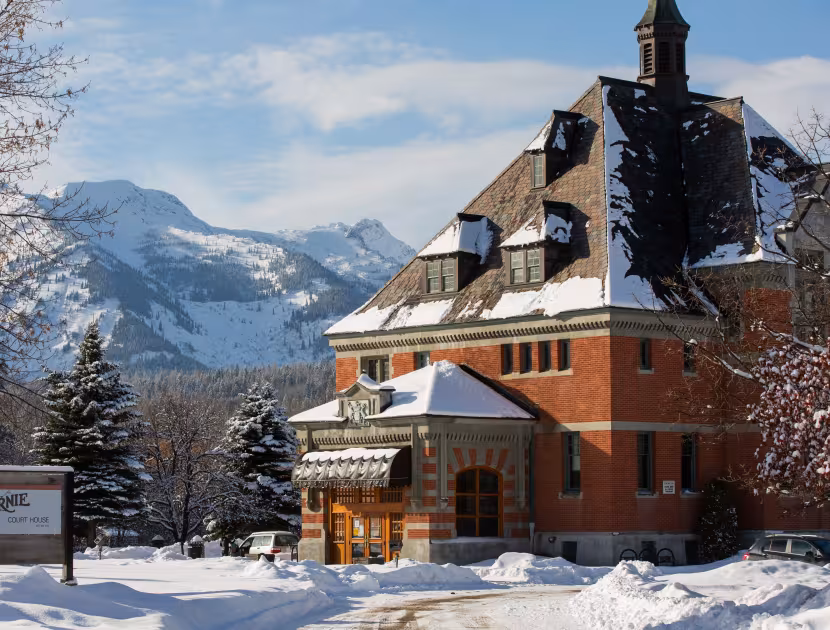 Snow-covered red brick building with mountain range in background.