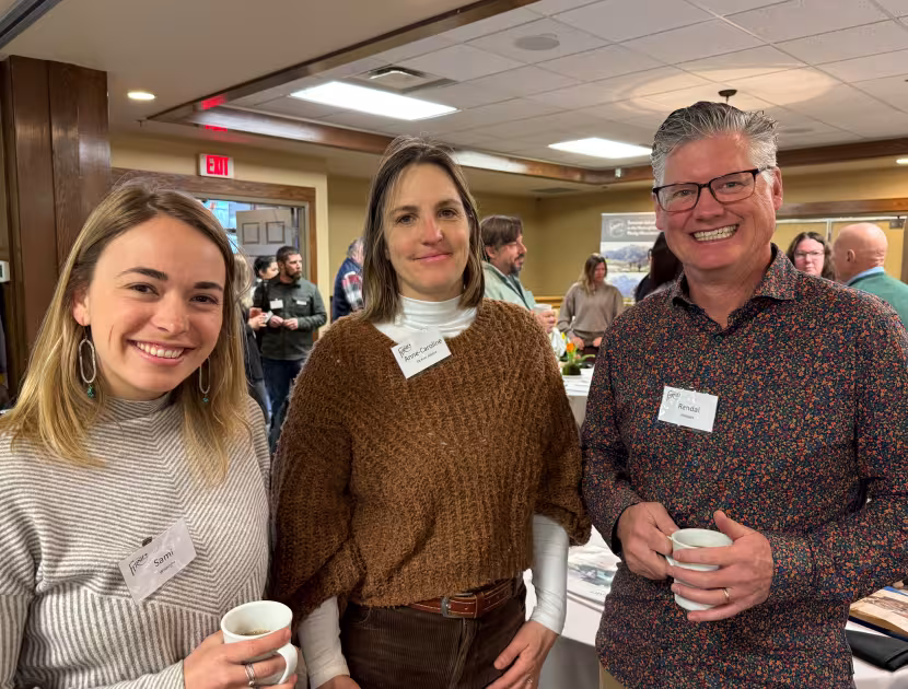 Three people smiling and holding cups of coffee at a gathering.