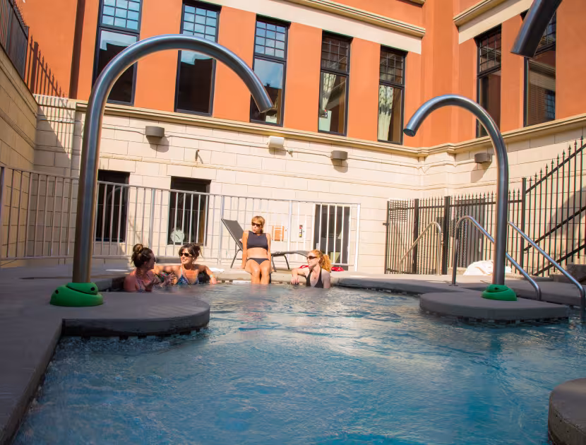 People lounging by an outdoor hot pool with metal jet structures.