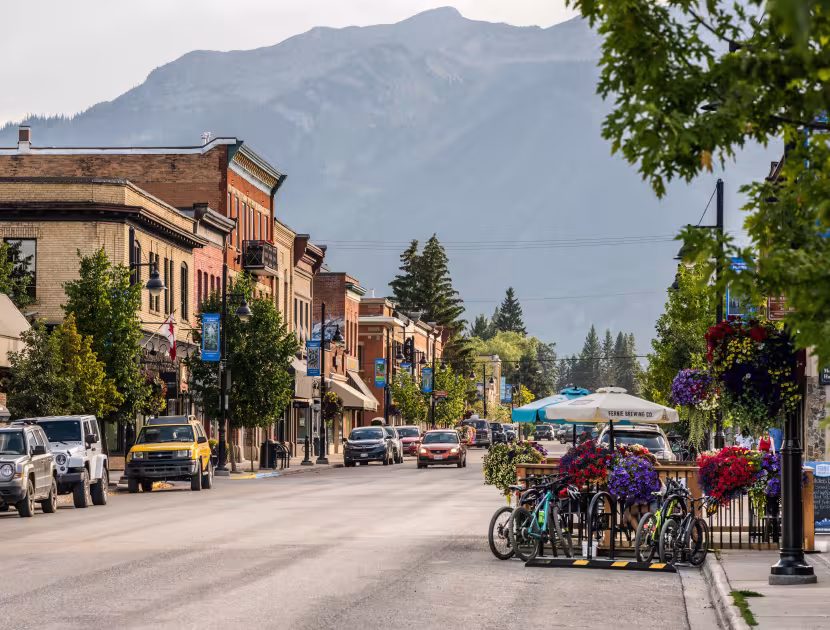 Quaint town street with mountains in the background, colorful umbrellas, trees, and parked cars.