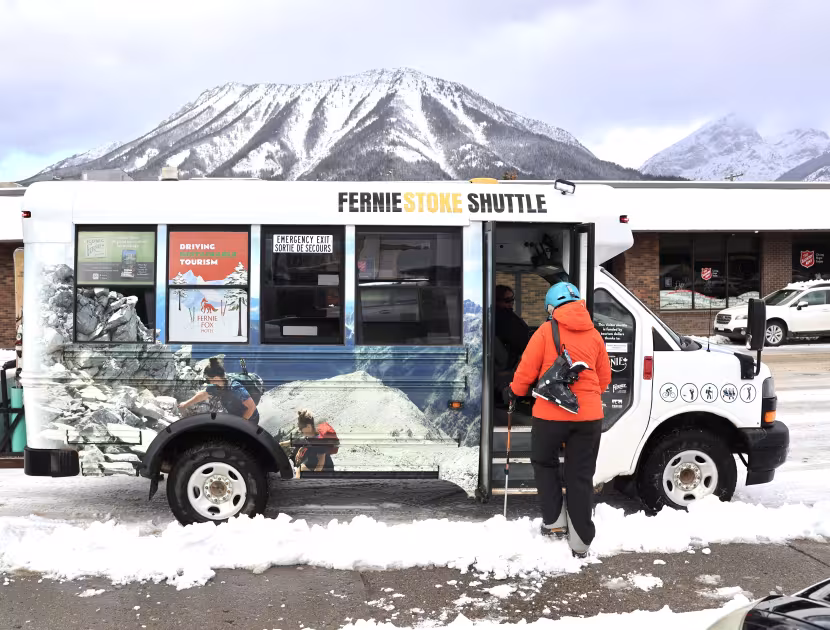 Person in orange jacket boarding snowy shuttle bus with mountain view.