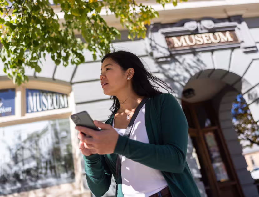 Woman in green sweater holding a phone outside museum.
