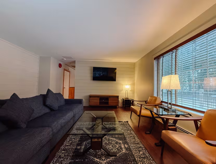 Cozy living room with gray couch, wooden furniture, and large window overlooking cityscape.