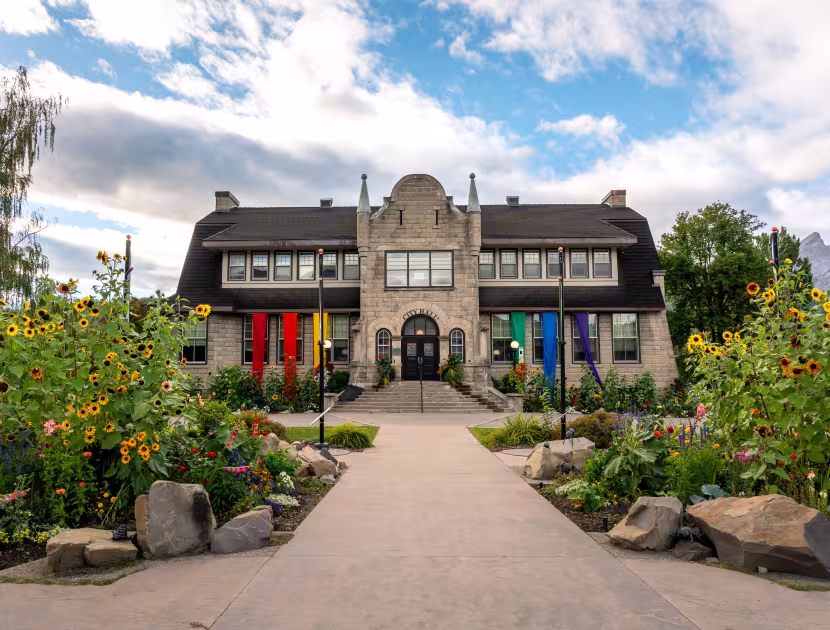 City Hall building with colorful flags, surrounded by garden and walkway, blue sky with clouds.