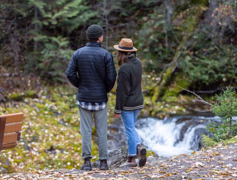 Couple standing by a small waterfall, looking out at a stream.
