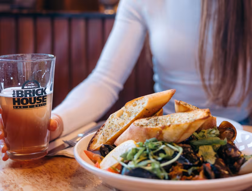 Woman sitting at a table at the Brickhouse Bar & Grill with a plate of food and a pint glass.