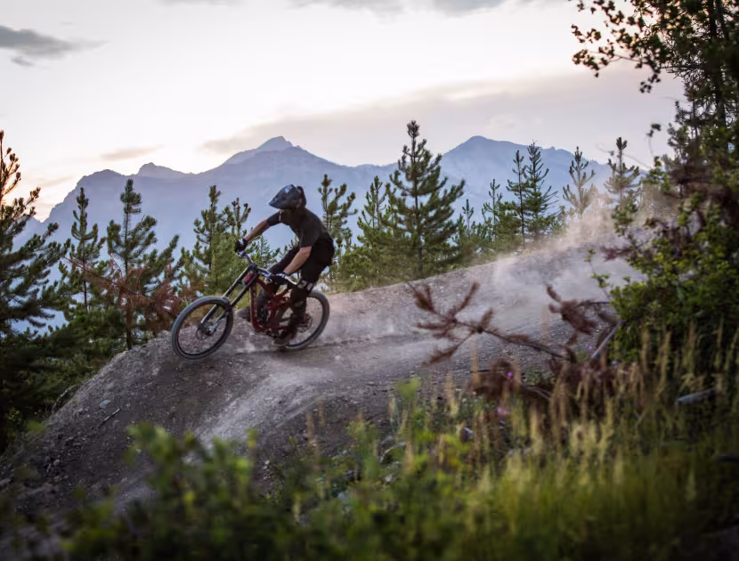 Mountain biker riding down a dirt trail surrounded by trees and mountains in Ridgemont area in Fernie..