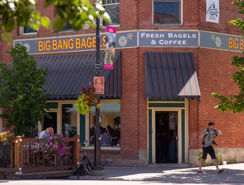 A brick storefront of Big Bang Bagels with outdoor seating; person walking on sidewalk.