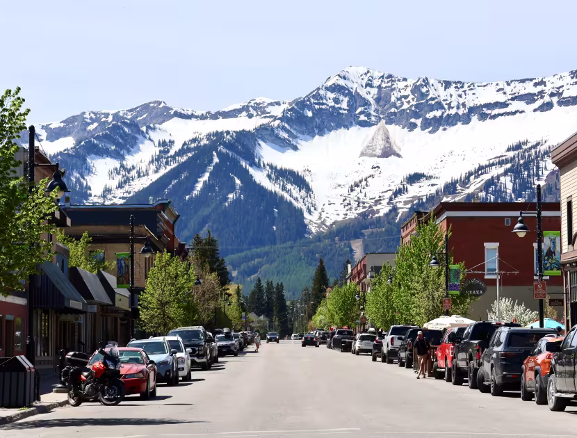 Snow-capped mountains behind Fernie's Historic Downtown 2nd Avenue with parked cars and heritage buildings.