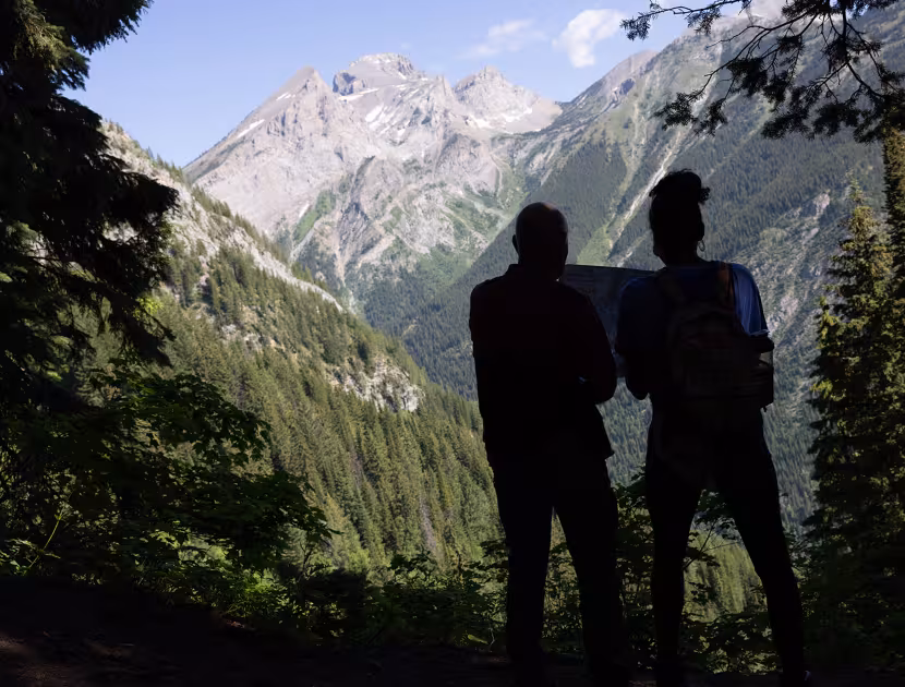 Two silhouetted people standing at the Mt Fernie half-way lookout, with Three Sister mountain in the background.