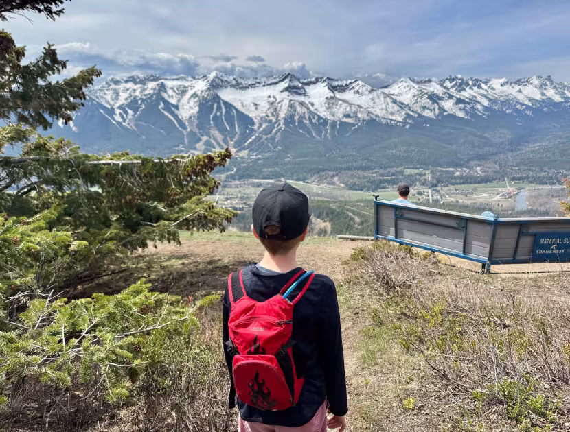 Person with a red backpack facing away from camera looking at snowy mountains of the Lizard Range in Fernie.