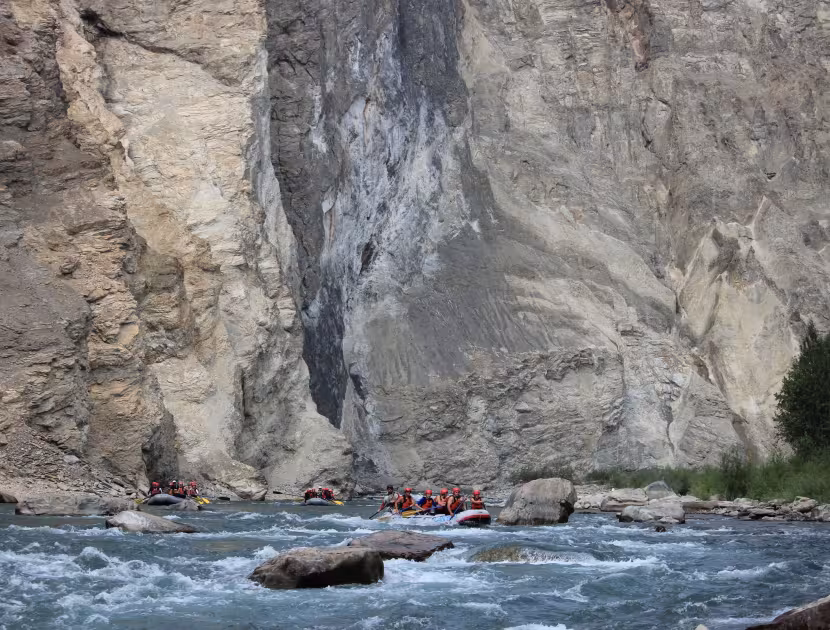 People in orange life jackets rafting on the Elk River with rocky cliffside.