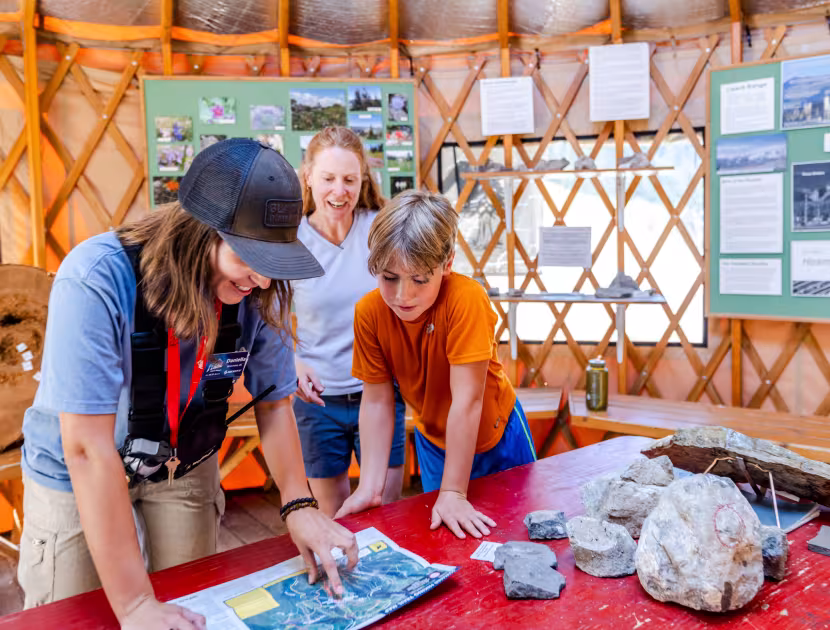 Three people gathered around a red table, looking at a map and rocks.