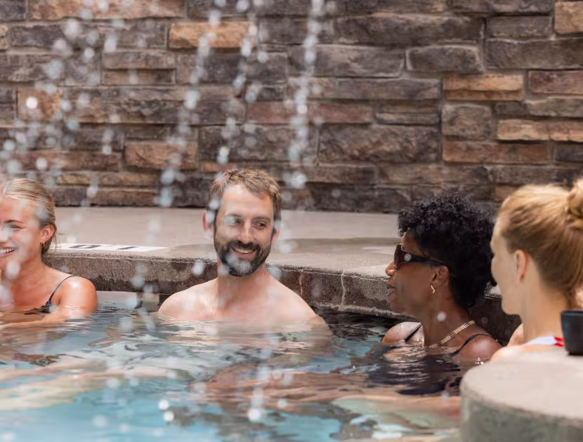 Four people smiling while in an outdoor hot pool with a waterfall feature.