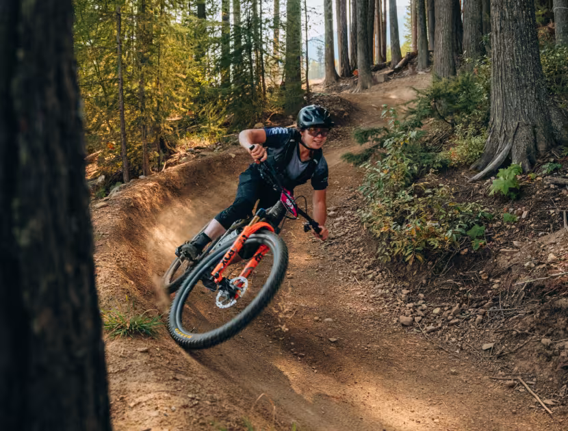 Cyclist on orange bike navigating a dirt trail through a forest.