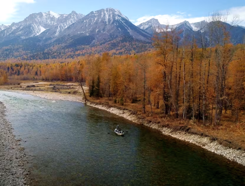 Serene river flowing through autumnal landscape with snow-capped mountains.