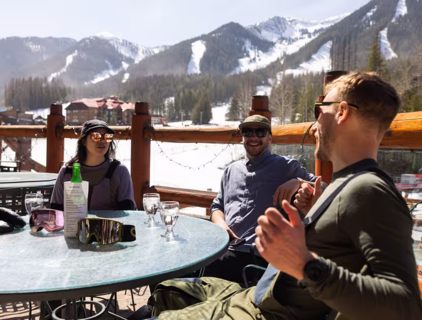 Three friends dining outdoors on a snowy mountain patio.