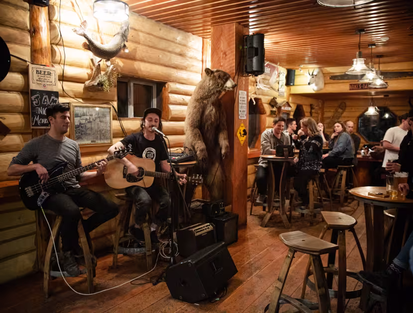 Live musicians perform in a warm, wood-paneled bar as patrons watch.