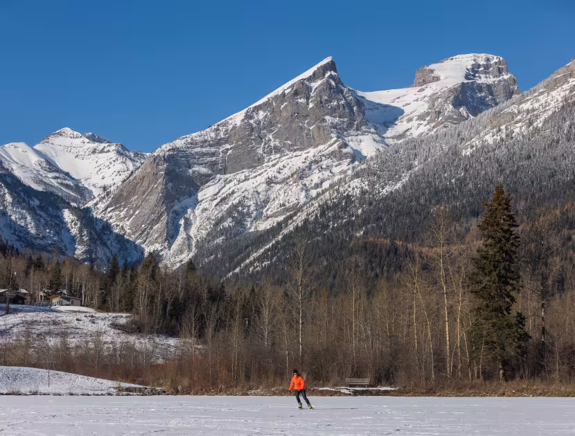 Snow-covered mountain valley with a person ice skating on a frozen, snow covered lake.