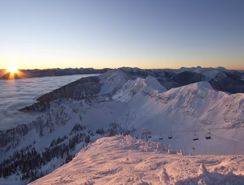 Sunrise over snow-covered mountain peaks and ski slopes.