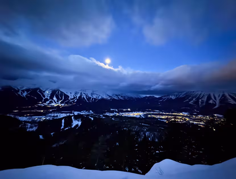 Moonlit snowy mountains overlooking a valley of glowing town lights