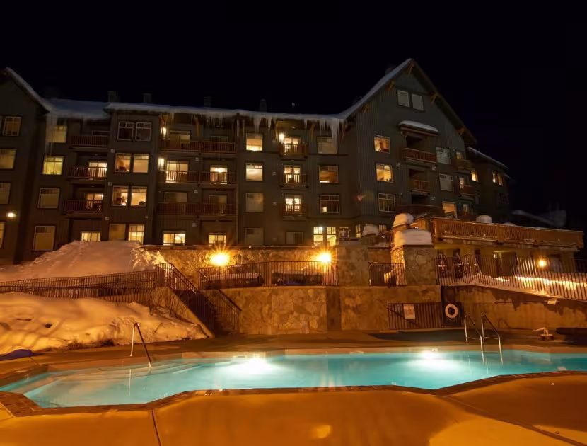 Illuminated Snow Creek Lodge hotel overlooking a glowing outdoor pool at night, surrounded with snow.